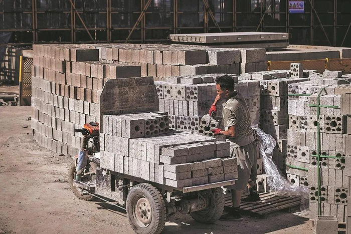 图为未戴安全帽的工人在项目工地搬运防火建材