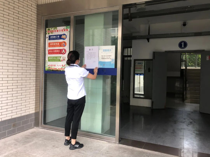 物业中心人员在宿舍楼栋门口张贴限制流动告示
