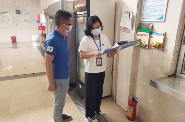 （始兴县市场监管局执法人员检查学校食堂台账记录。邹兰 摄）