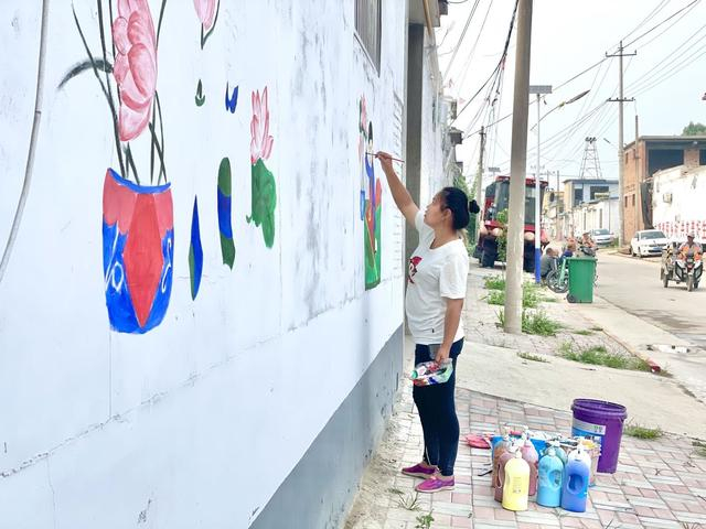 刘师一手拿着调色盒,一手拿着画笔在墙壁上作画。新京报记者 耿子叶 摄