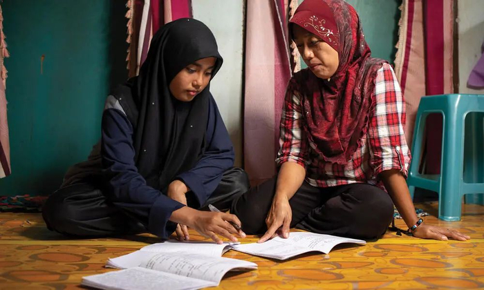 Arni Mansur 和她的女儿一起复习家庭作业，她在父母工作的种植园上学。© AARON GEKOSKI/WWF-US