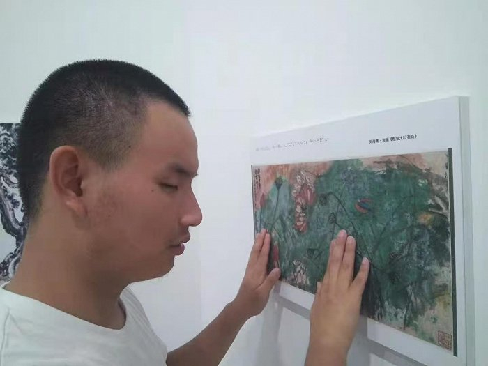 胡华健在“触摸光影”非视觉摄影展上欣赏作品。受访者供图 .jpg