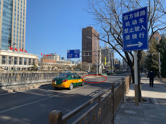 ▲人行道旁立有“前方辅路机动车禁止驶入请绕行”的提示牌，黄色箭头所指为机动车禁行标志，红圈处为路面右拐指示。新京报记者 李睿阳 摄