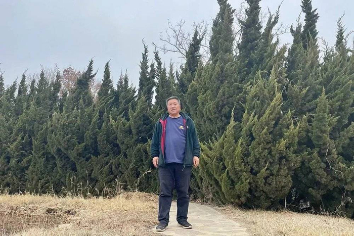 孙洪奎穿着爱丁堡皇家植物园的工作服，站在龙柏前 ©胡卉 摄