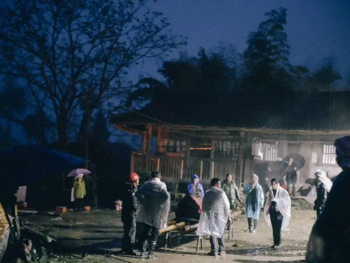 天上下着雨，棺材从堂屋放到院子中间，人们准备出发。