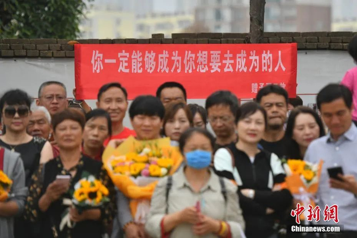 资料图：6月8日，云南省昆明市的考生结束2021年全国高考。图为考试结束后，一幅助考标语前有考生和家长合影留念。中新社记者 刘冉阳 摄　