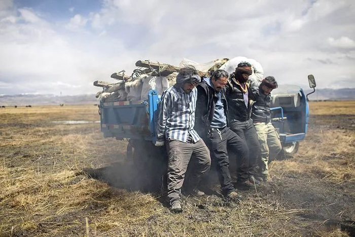 ▲2021年4月23日，雨后，先前运送物资的小货车陷在了草场上。扎琼巴让和牧民们用力抬起货车一侧，但车轮仍然在泥泞中打滑，车身动弹不得。