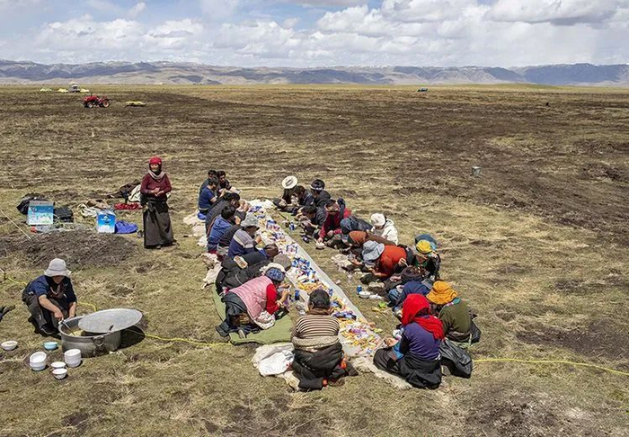 ▲4月24日下午1时，部分牧民回到营地。一块塑料布上，摆满了各种零食、饮料、肉类、水果，大家席地而坐。一旁，负责后勤的牧民为每一位劳动者，端上牦牛肉汤面片。