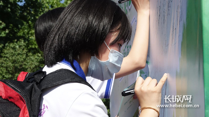 参加活动的同学们在活动背板上签下自己的名字，承诺从我做起，保护自然。长城网记者 李代姣 摄