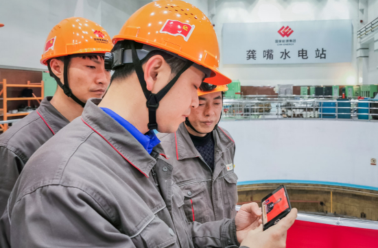 在国家能源集团大渡河公司龚嘴水电站，员工在检修现场，利用工作空隙，通过手机观看开幕会。张燕 摄