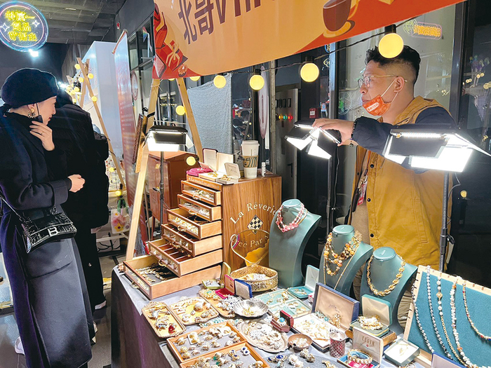 在创意饰品摊位前，一位消费者正在试戴耳环。