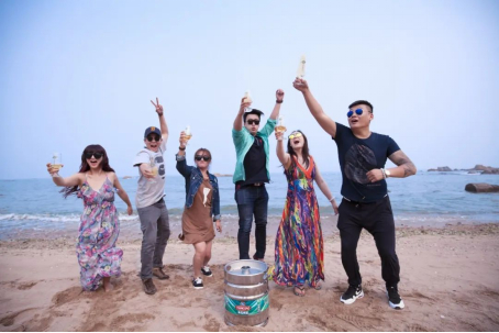 游客们在海边举杯畅饮，他们面前放置的是青岛啤酒十升桶。