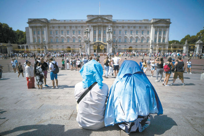 　　7月18日，英国伦敦，白金汉宫外，人们坐在那里捂着头以免被太阳晒伤。 视觉中国供图