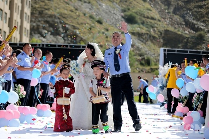 图为8月5日，“边守·边爱”集体婚礼现场彝族民警胡文宇和藏族妻子次旦央宗在战友们祝福中走向舞台 摄影：何宇恒