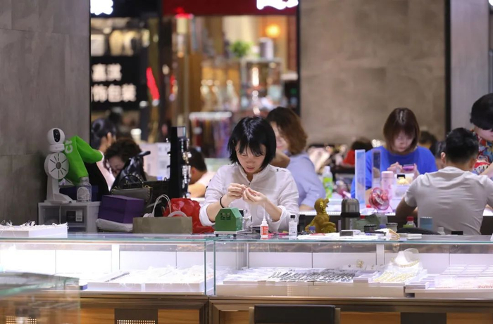 ▲&nbsp;深圳水贝某珠宝卖场内，一位店主一边卖货一边做手工。图 / 视觉中国