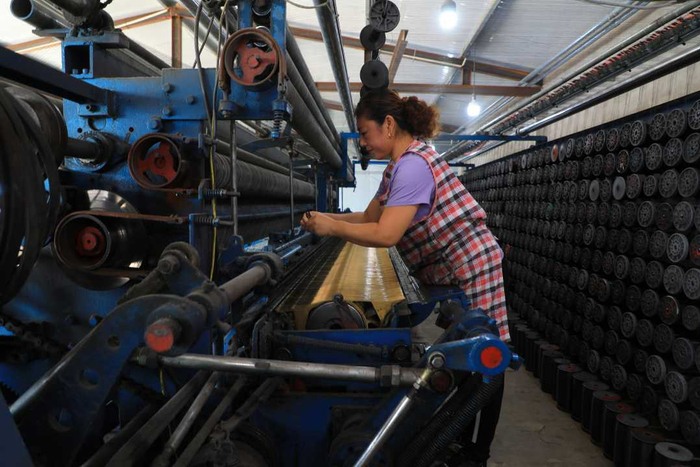 工人在河北省滦南县程庄镇东胡家坡村一家网具加工企业织网机上接线。