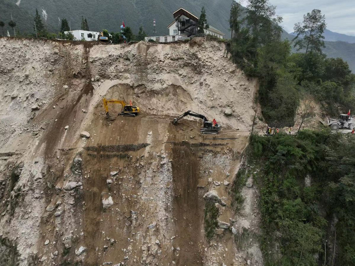 9月6日，泸定县磨西镇通往海螺沟景区的道路被山体滑坡阻断，蜀道集团工作人员通过挖机在绝壁之上全力抢通道路。（杨树 摄）