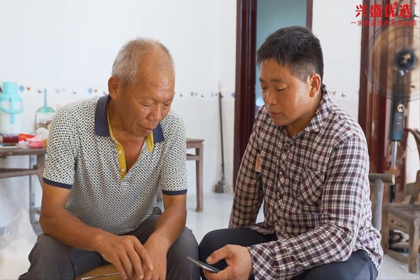 　　图为门店老板康福初教村里老人使用兴盛优选小程序购物