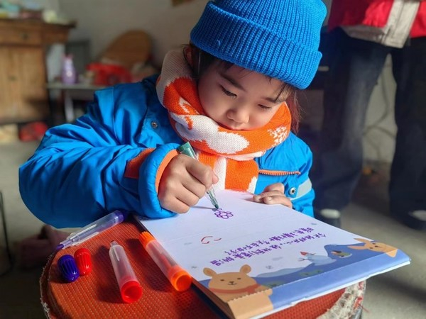 　　小朋友用温暖包里的水彩笔写下“冬天不怕冷了”