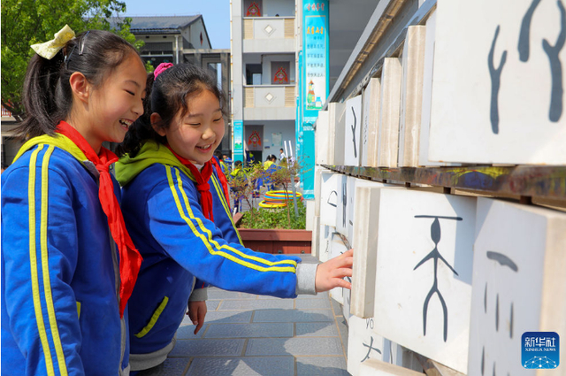▲2022年4月18日，安阳市第一实验小学学生在甲骨文文化墙旁学习甲骨文。图/新华社