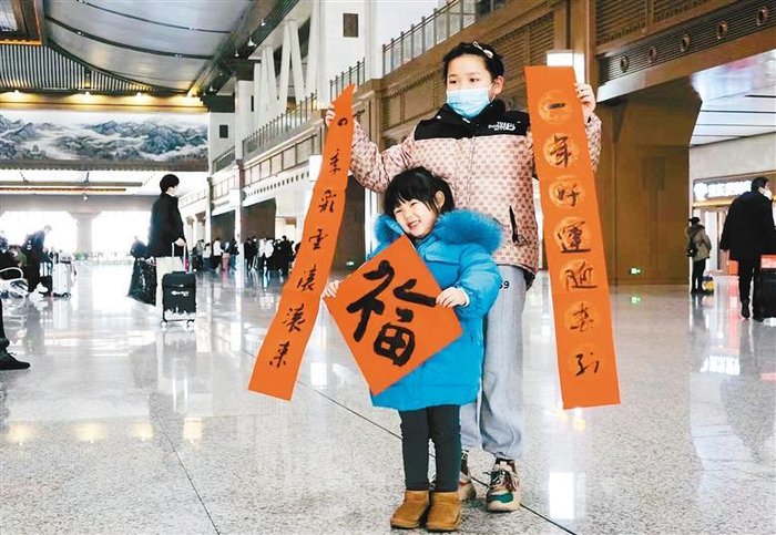 在西安站候车大厅内，两位小朋友展示春联和“福”字，准备和家人一起乘车回家。（记者 翟小雪 摄）