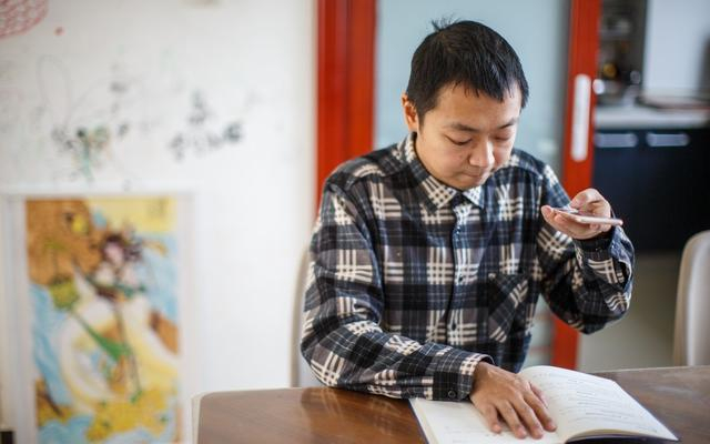 蔡聪在家中阅读纸质书时，使用手机的识别软件将书中内容转化为语音。新京报记者 王子诚 摄