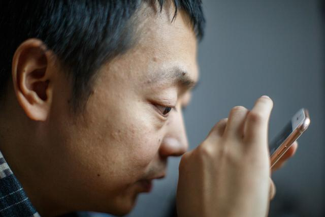 蔡聪在家中用手机寻找照片，照片无法转化成语音，他只能努力靠近屏幕辨别画面。新京报记者 王子诚 摄