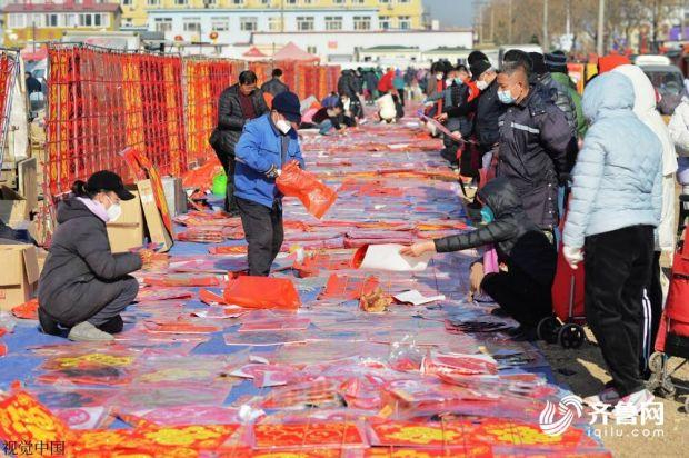 图/12月30日，青岛，城阳区上马街道年货大集上，市民在摊位前选购对联、福字。