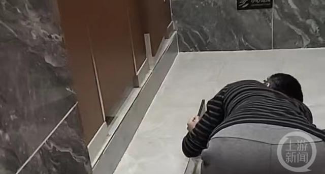 ▲嫌疑人在女厕所里跪地偷拍。图片来源：视频截图