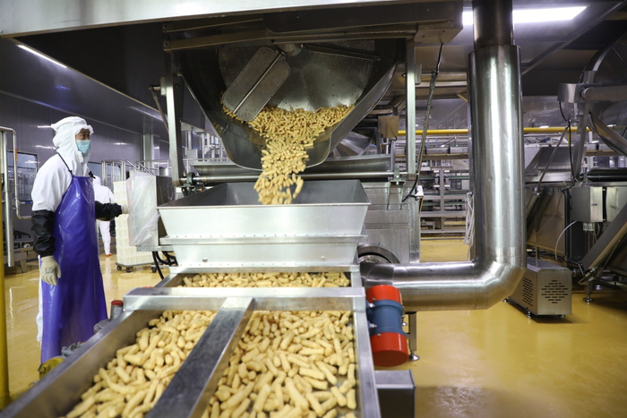 图为香河县丰丰食品有限公司，工人将油炸好的鱼段倒入生产线内。