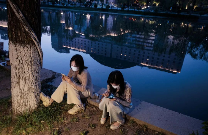 2022年5月2日，北京。亮马河畔，两位女性坐在一起看手机。｜图源视觉中国