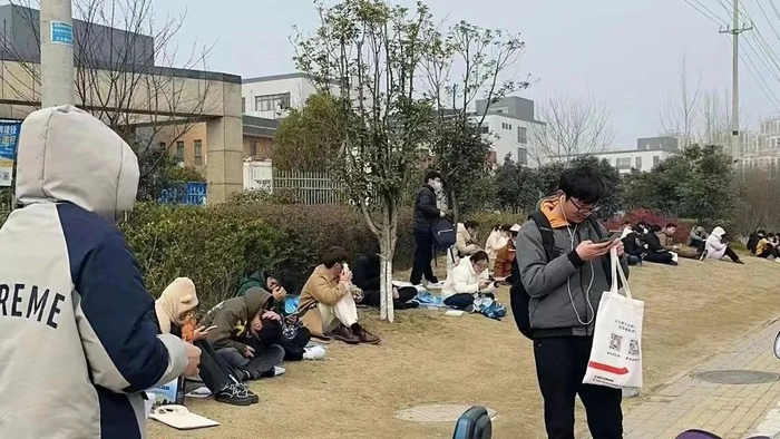 2月25日合肥市一考场外的考生，许多考生中午选择不回酒店，直接在学校旁边的草坪坐着等待。图/受访者供图