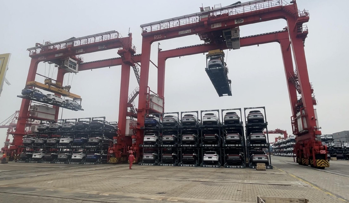 码头龙门吊正堆叠已装箱并绑扎好的汽车框架箱，等待装船（财联社记者拍摄）