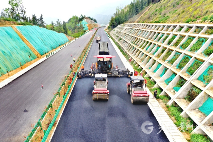 施工现场，沥青摊铺机缓速前进，压路机紧随其后