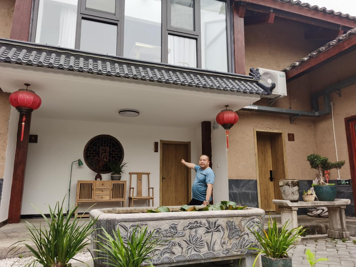 王学贵的身后是曾经破败不堪的百年老屋。（王莉莉 摄）