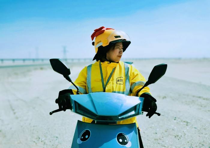 ▲90后外卖女骑手罗琴，身后是环塔克拉玛干沙漠铁路桥。（摄影：施安）