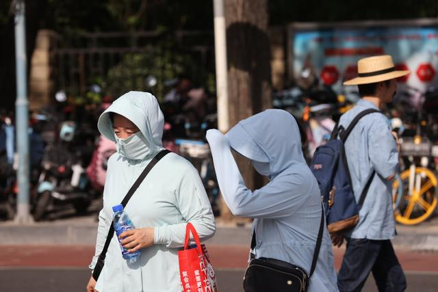6月27日，北京三里屯，市民身着防晒衣走在阳光下。  新京报记者 王子诚 摄