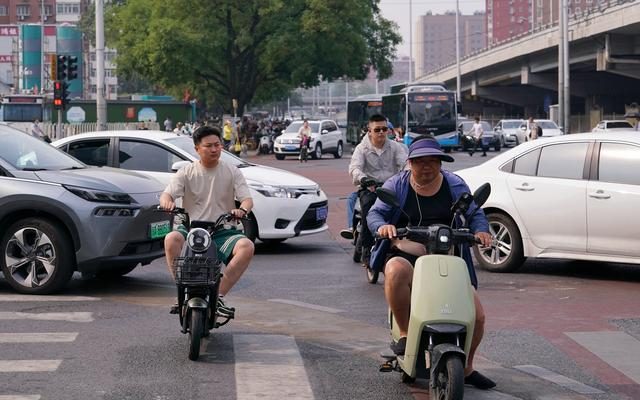 双井路口，几名没有佩戴安全头盔的骑行者从车缝中穿行。新京报记者 王贵彬 摄