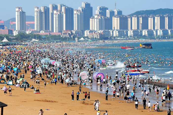 ↑7月5日，青岛金沙滩海水浴场，游客在海滩亲水消夏 图据视觉中国