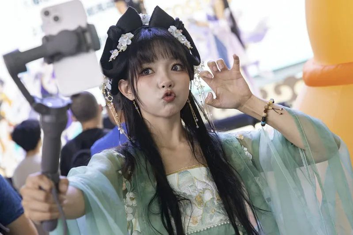 张欣羽拿着自拍杆拍摄舞台上的coser表演。
