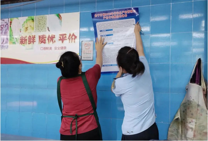 图为猪肉经营商户与执法人员张贴《关于开展2023年非法生产经营猪肉产品专项整治的通告》