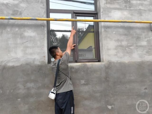 ▲岳旭在用手比划救援船进村时磕到了窗边。图片来源/上游新闻记者 张锦