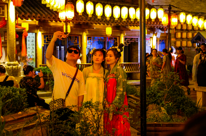 夜色下的洛阳洛邑古城灯火璀璨，身着汉服的游客在古城内自拍。中国旅游报记者 曹雪文 摄