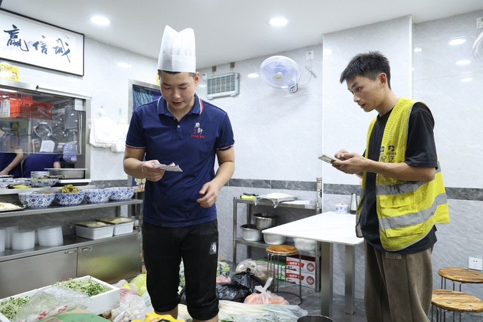 ▲图为食材配送员和店员核对线上订单 摄影/朱冲