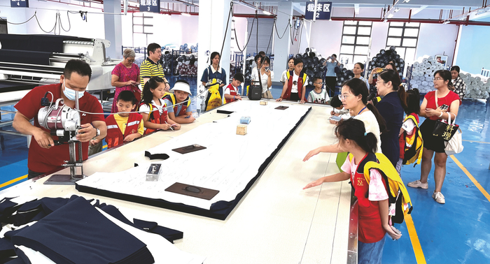     ▲小记者们在裁床生产线了解布匹裁片情况    本报记者 覃祖稳 摄