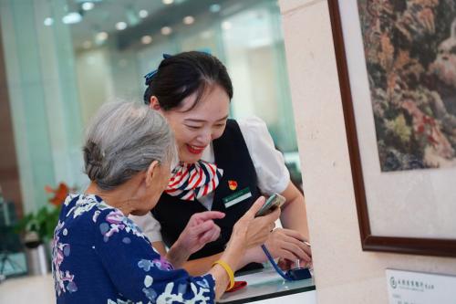 老年客户在成都农商银行总行营业部青年党员的指导下使用“关爱版手机银行”。（刘晓月 摄）