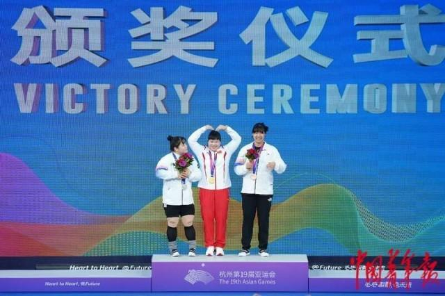 10月6日，杭州亚运会举重女子87公斤级决赛颁奖仪式，梁小梅（中）向现场观众比心。中青报·中青网记者 赵迪/摄