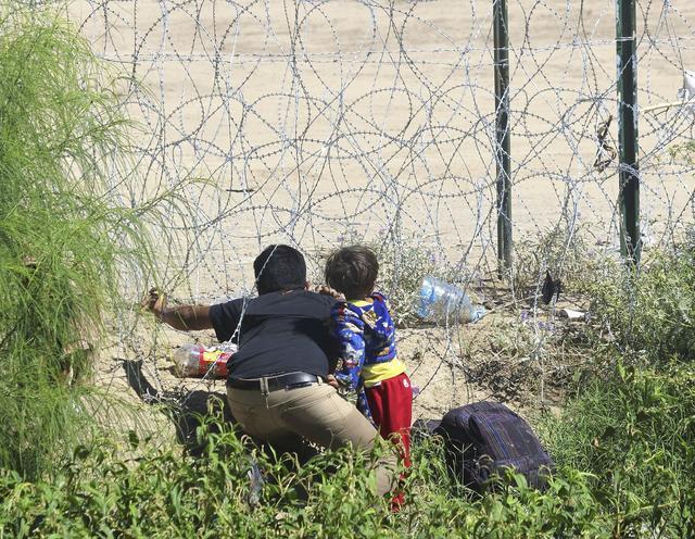 当地时间2023年9月29日，美国埃尔帕索，一名带着孩子的男子拿着刀片穿过铁丝网，边境警卫将他拦住。图/视觉中国