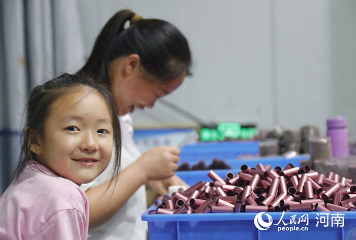 村民郭艳秋带着孩子在家门口的扶贫车间工作。人民网 霍亚平摄
