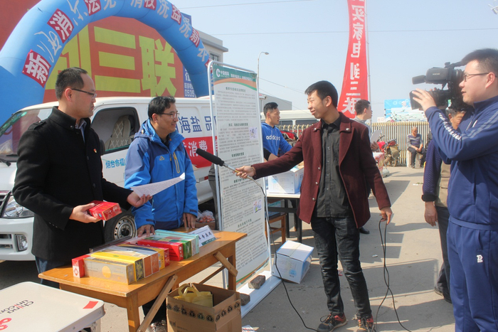 图为普法志愿者在福山大集入口开展真假烟鉴别讲解，并接受电视台采访
